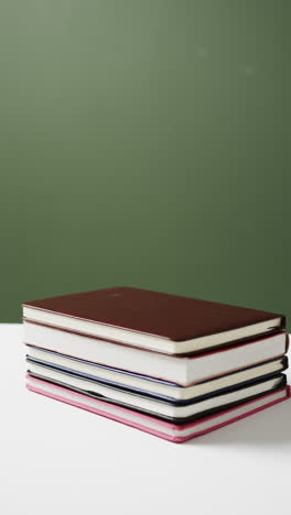 vertical video of stack of books with copy space on green background, in slow motion