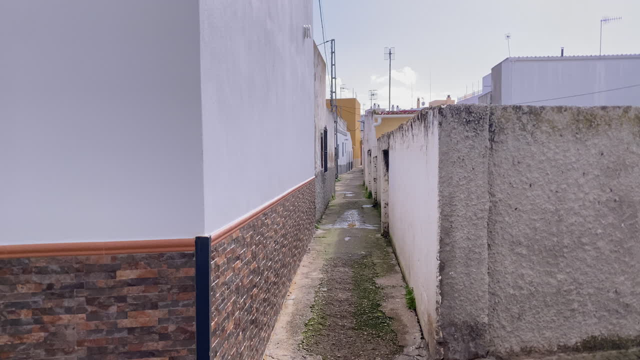 Stretto vicolo che si snoda tra edifici residenziali, riflettendo il paesaggio urbano e l'architettura tradizionale di una città andalusa.