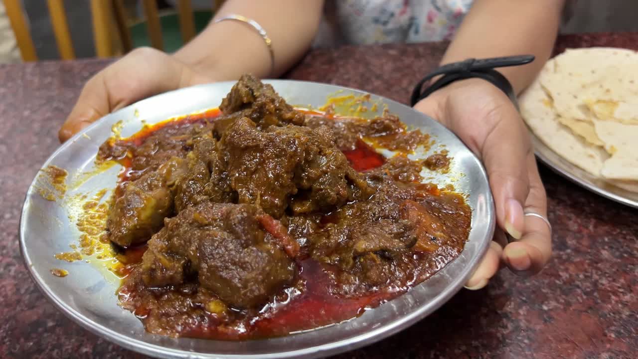 A girl holding a steel plate full of spicy mutton curry in a Dhaba in Kolkata. No face video.