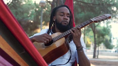 ethnic guy playing guitar in hammock in countryside