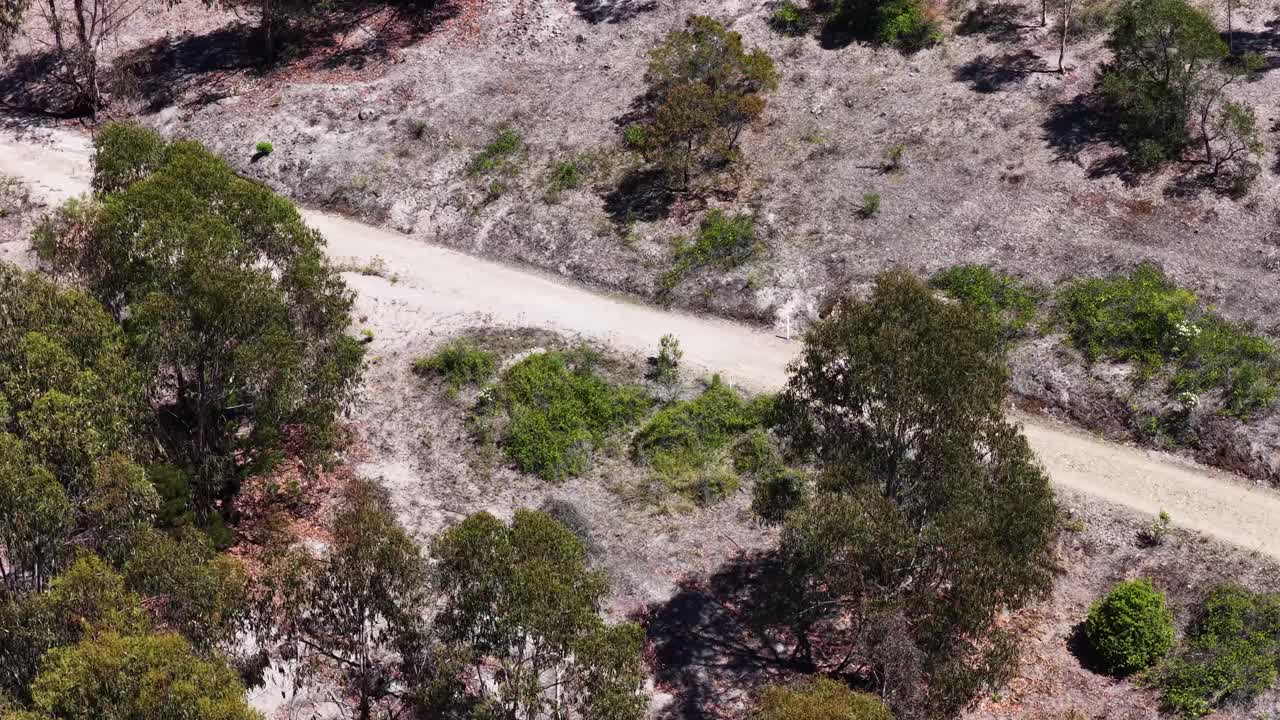 En droneoptagelse i fugleperspektiv følger en ensom cyklist, der kører ad en snoet bjergsti af jord