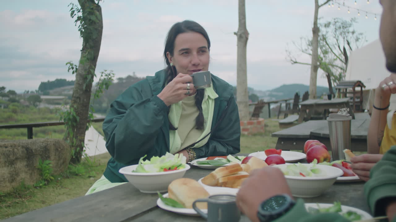 Girl Drinking Tea and Speaking with Friends over Dinner at Campsite