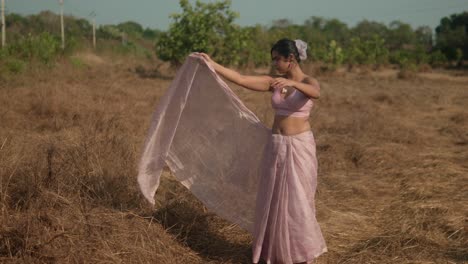 Mujer-Con-Traje-Tradicional-Rosa-Bailando-En-Un-Campo-Seco,-Soleado-Telón-De-Fondo-Rural