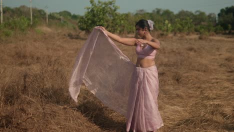 mujer con traje tradicional rosa bailando en un campo seco, con un fondo rural soleado