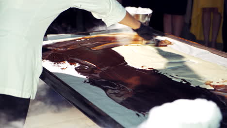 professional chef is making ice-cream and mixing black with white cream. close-up of cook's hands in black gloves preparing delicious dessert on a big board.