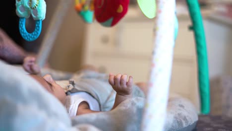 Adorable-Newborn-Baby-Girl-Laying-Down-in-Cradle-and-Looking-at-Colorful-Toys