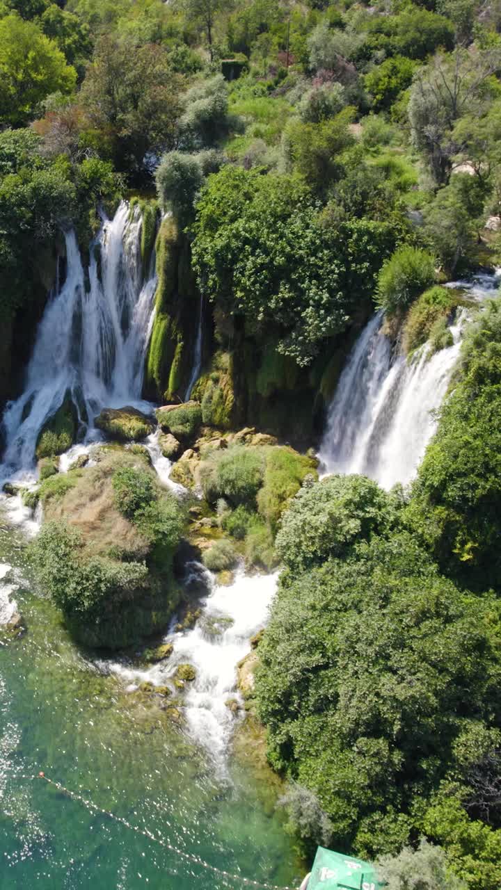 Cascata di Kravica che scorre su rocce muschiose e circondata da una vegetazione rigogliosa. Avvicinamento aereo, video verticale