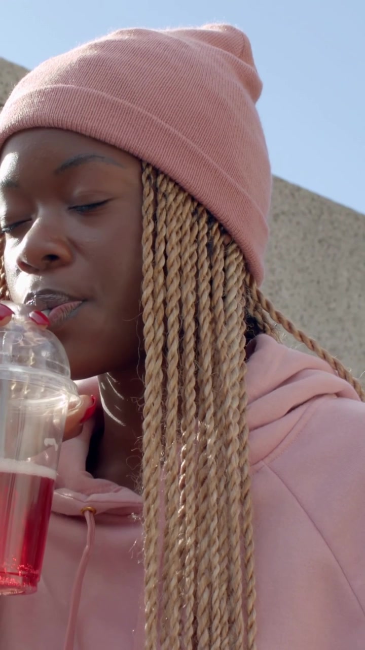 Vidéo verticale : Déjeuner, femme en bonnet et sweat à capuche sirotant une boisson rouge avec une salade sur un muret, espace pour le texte.