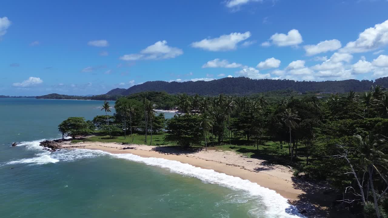 Aerial drone footage of a hidden tropical beach in Koh Lanta, Thailand, featuring swaying palm trees, rugged rocky coastline, golden sand, and clear blue water, with no people