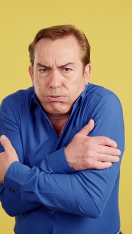 man shivering and feeling cold on a yellow background