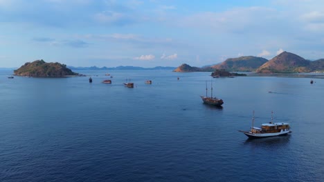 Wide aerial view of numerous traditional boats anchored in deep blue waters near Komodo’s hilly islands