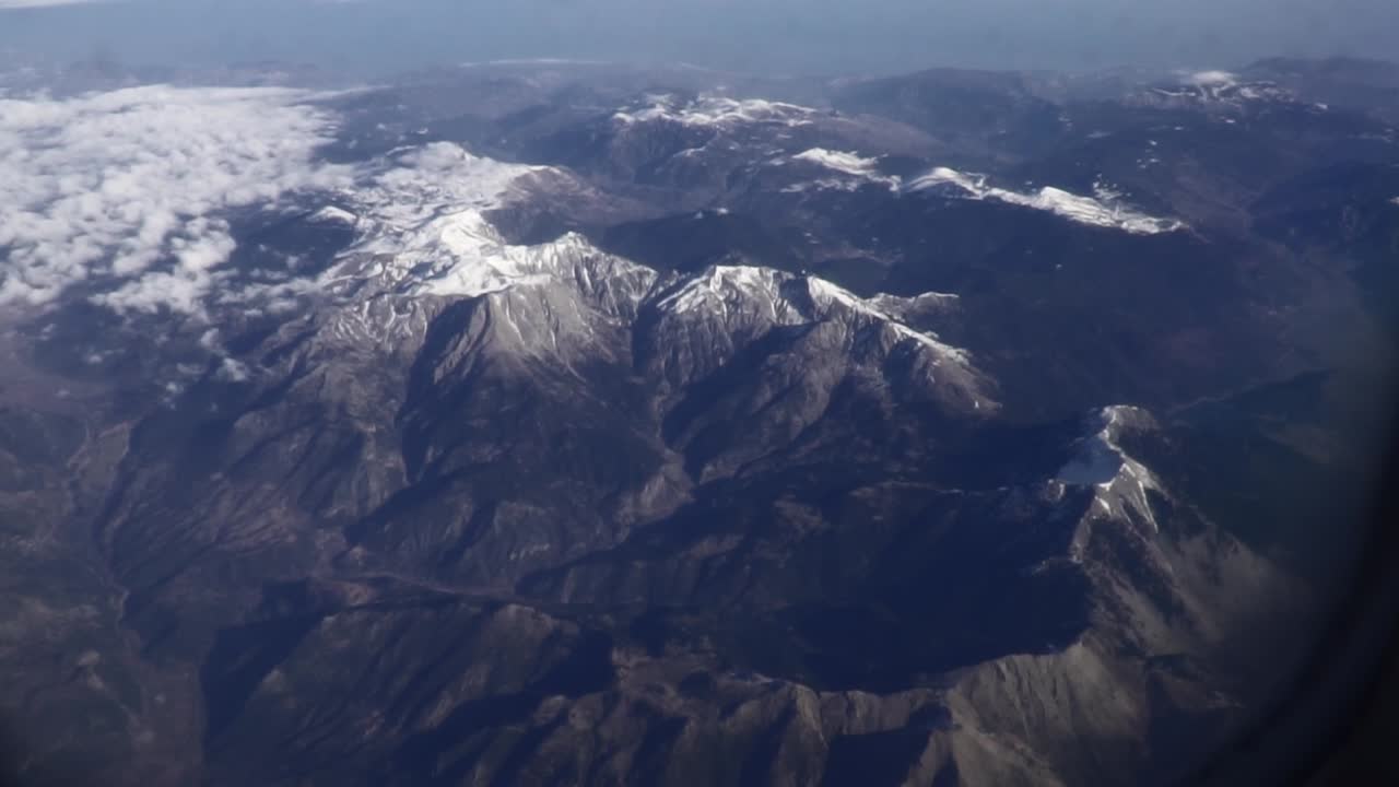 toma panorámica desde la ventana de un avión que muestra las montañas griegas cubiertas de nieve