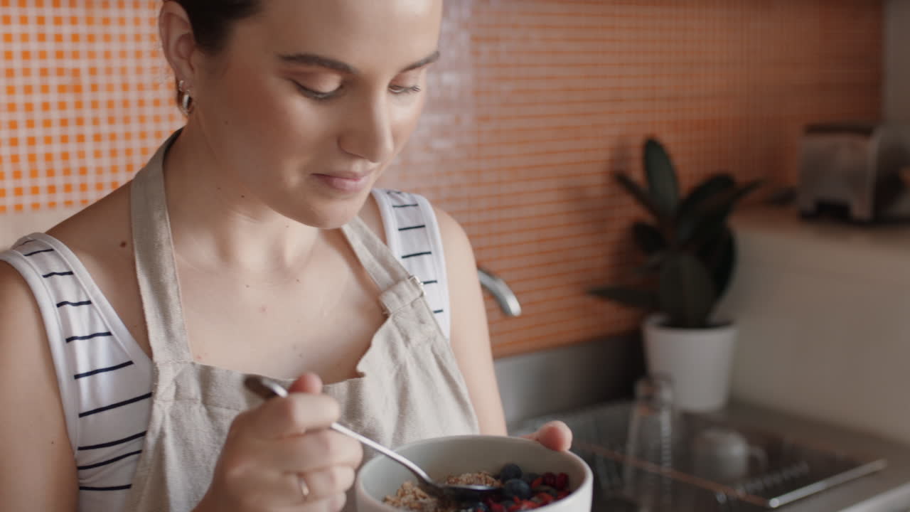 giovane donna felice a fare colazione in cucina a gustare cereali sani a base di farina d'avena miscelati con frutta rilassandosi a casa nel fine settimana