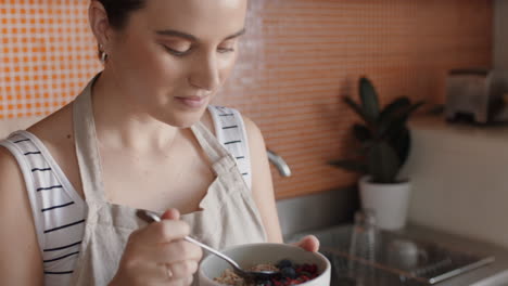 mujer joven feliz desayunando en la cocina disfrutando de un saludable cereal de avena mezclado con fruta relajándose en casa el fin de semana