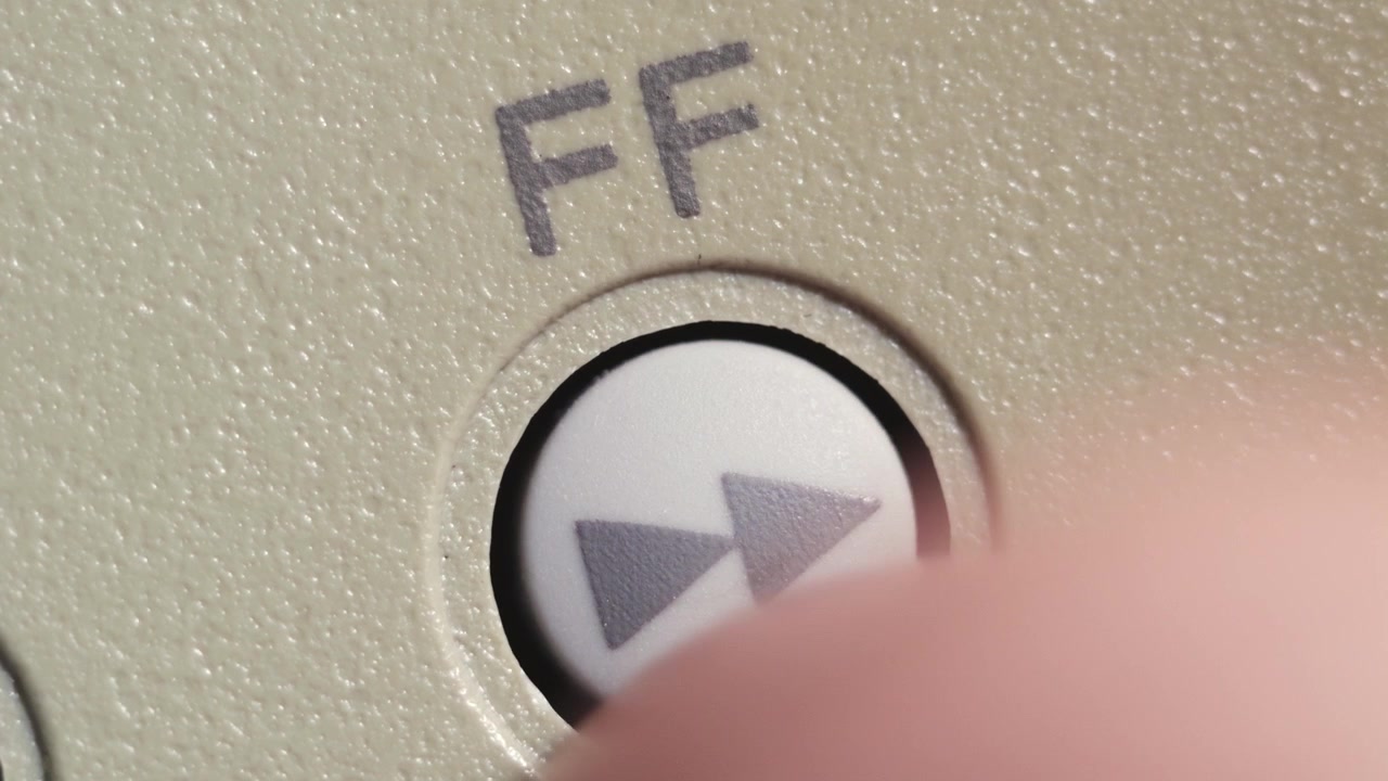 Angled macro shot of finger pressing white fast forward button on beige editing controller