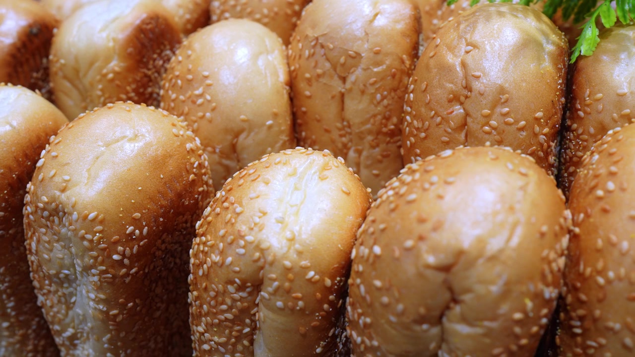 Primo piano di panini per hamburger con semi di sesamo disposti in file. Panini caldi, dorati e marroni con la superficie tostata che riempiono l'inquadratura.