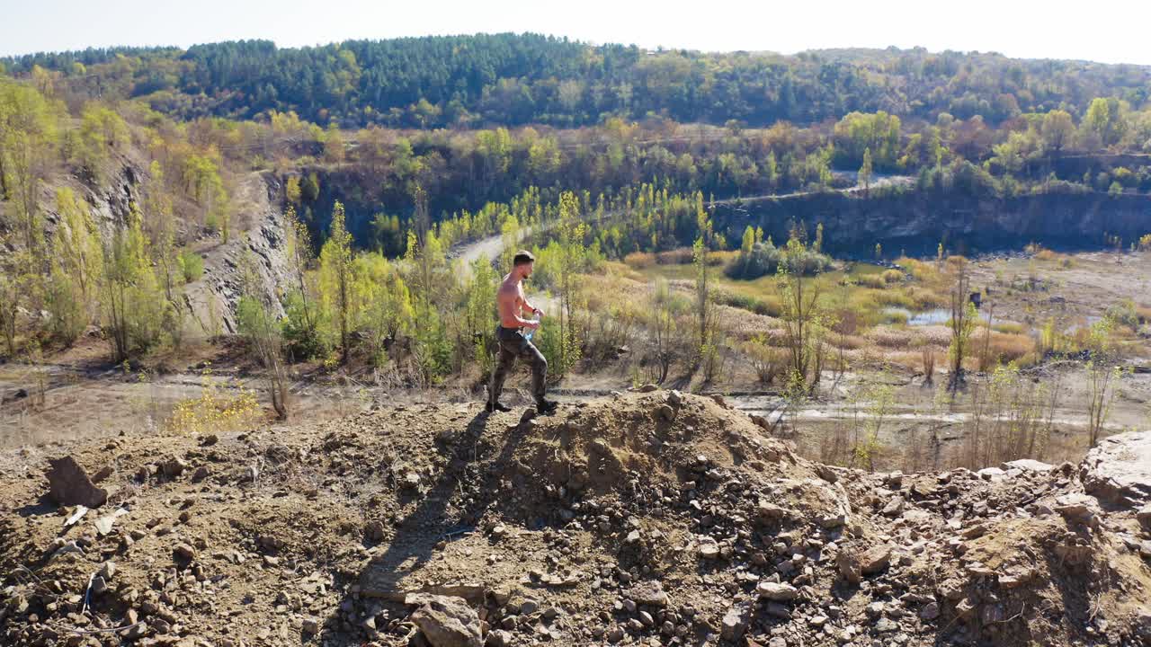 Shirtless sportsman walking in the canyon. Handsome athlete is drinking water on a beautiful nature background. Aerial view.