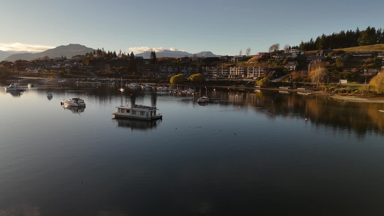 Low flight over wanaka lake in new Beamen during sunset time. Anchored boats and luxury waterfront apartments in New Zealand
