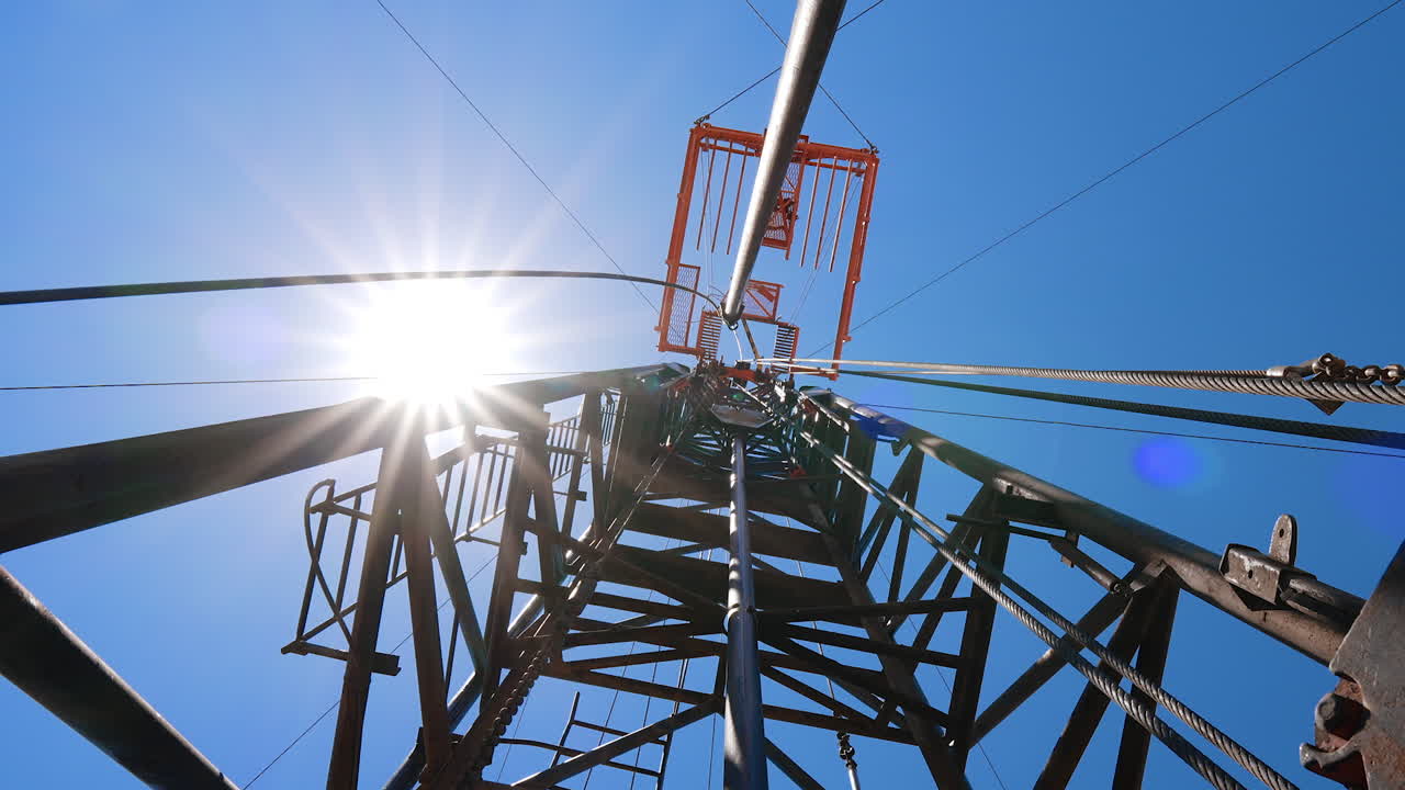 Standing at the tall tower for drilling natural resources. Low angle view. Derrick at the oil production site at the backdrop of blue sky.