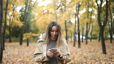 Junge-Schönheitsfrau,-Die-In-Einem-Herbstpark-Eine-Nachricht-Auf-Dem-Handy-Schreibt