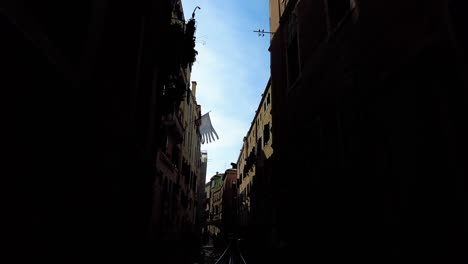 gondola boat sailing across canal river passing through old buildings at sunset in venice, italy