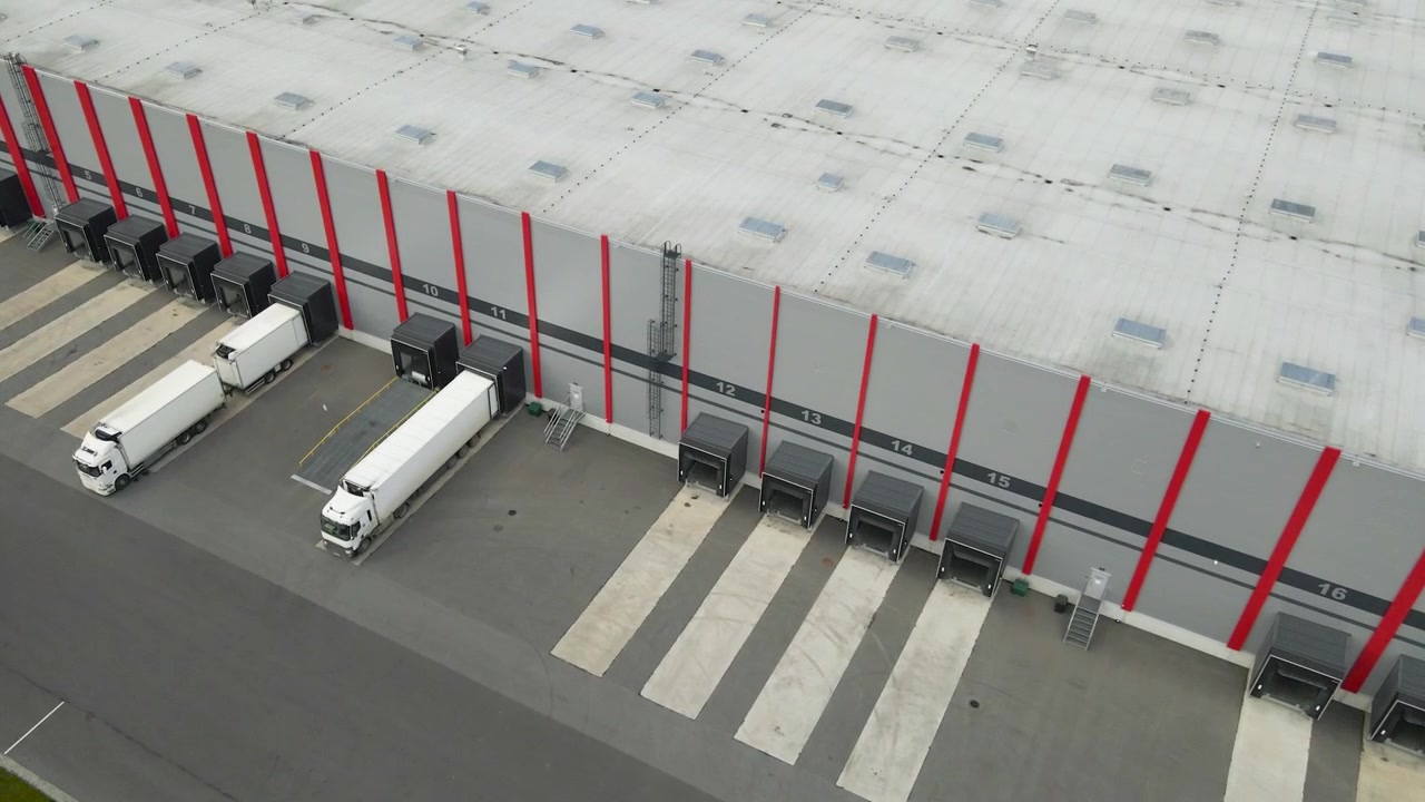 Højvinkelbillede af en sættevogn, der bakker ind til en læsserampe ved et moderne distributionscenterlager, klar til lastning af gods og global forsendelse i forsyningskædeindustrien