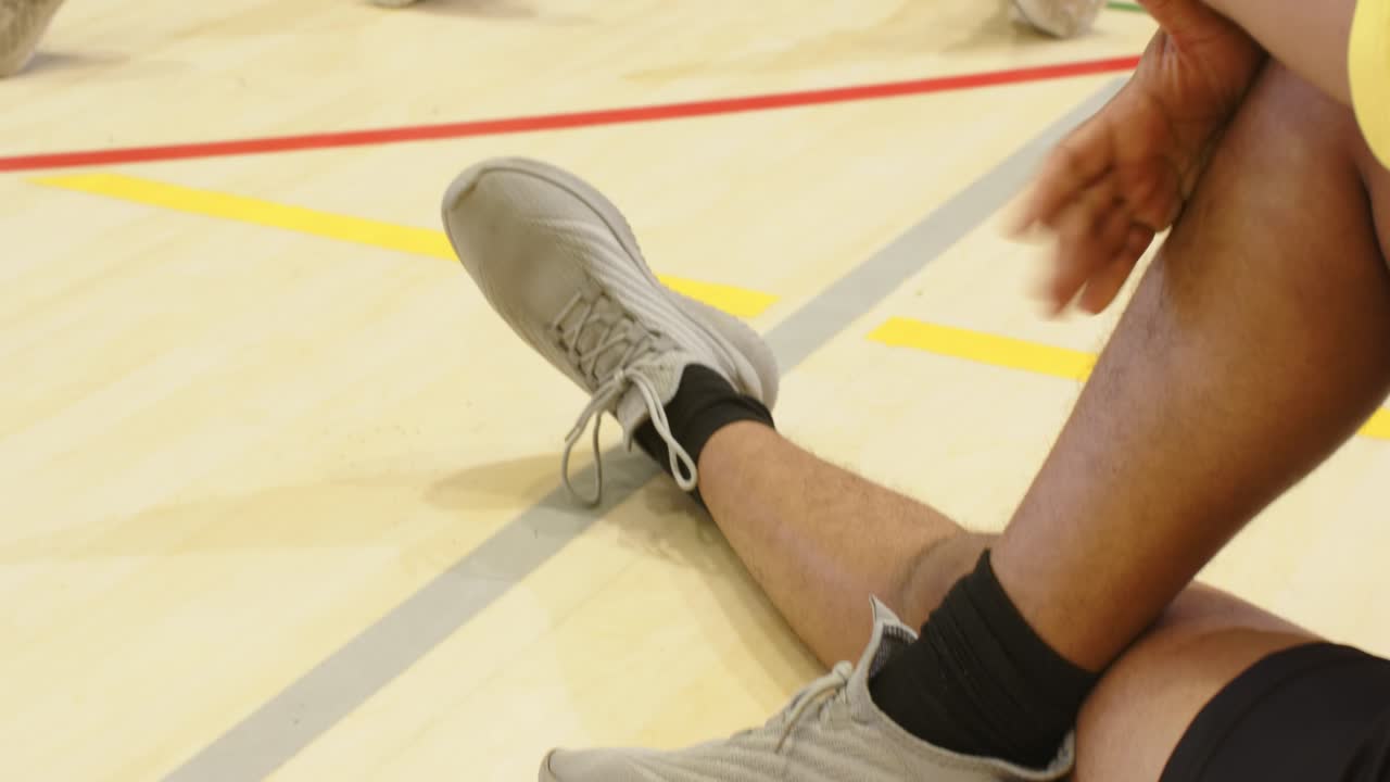 Diversi compagni di squadra uomini seduti in palestra dopo l'allenamento, che allungano le gambe attorno a una palla da pallavolo, con indosso magliette gialle.