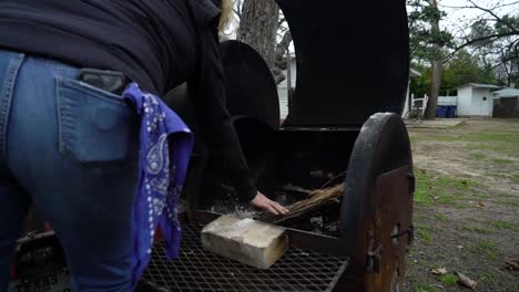 a women puts wood into a barbecue fire pit