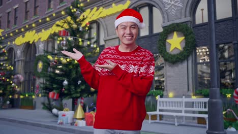hombre asiático en traje de papá noel con una sonrisa apuntando al lado mientras está de pie en la noche de navidad