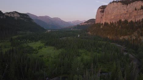 a lush valley with a river winding through dense forests at sunset, aerial view