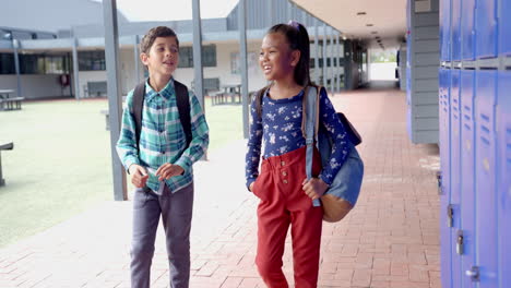 in school, two biracial students are walking by blue lockers