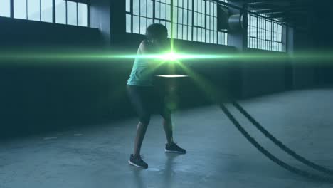 animation of shining light floating over woman exercising with ropes in an abandoned building