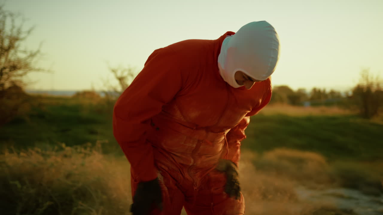 오렌지색 슈트를 입은 남성 우주 비행사가 유니폼에서 독성 오염 먼지를 흔들고 있습니다.