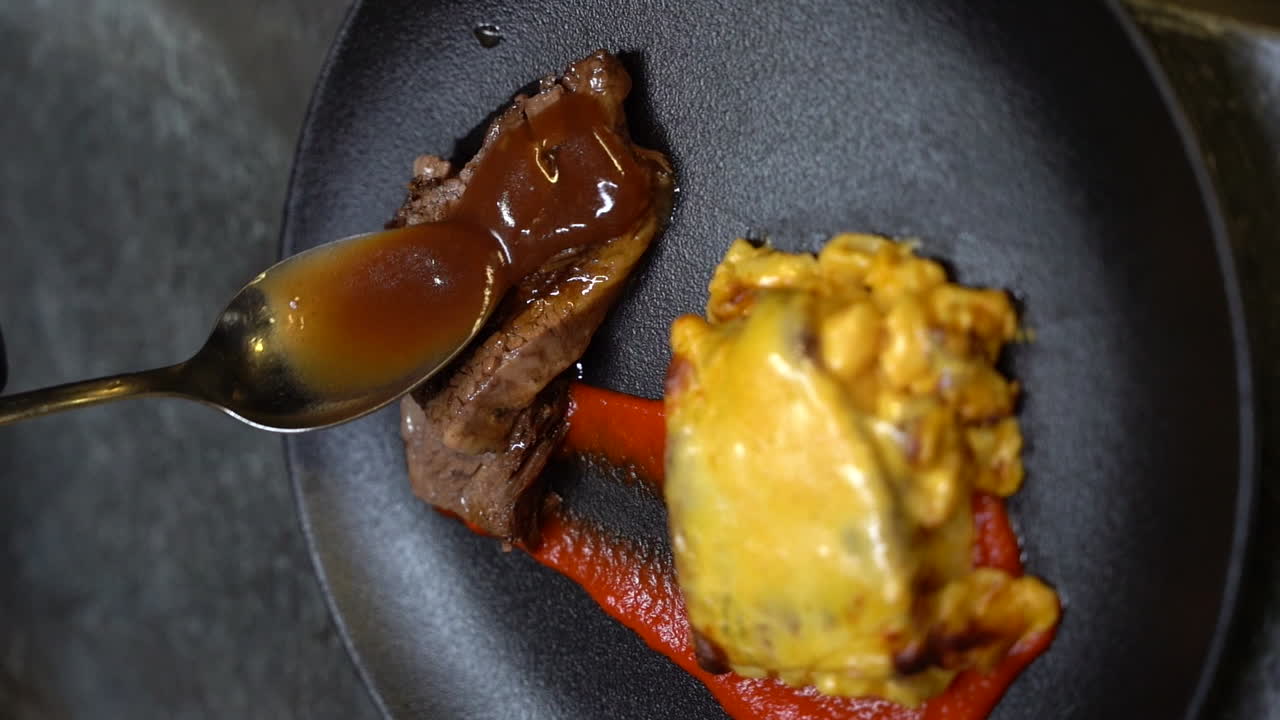 poniendo salsa en una rebanada de carne en un plato negro con macarrones y queso
