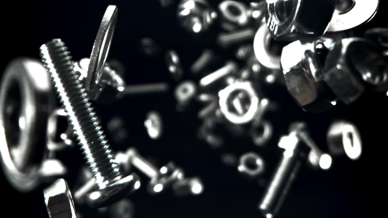 光沢のある金属製のボルト、ナット、ワッシャーがスローモーションで落ちる
