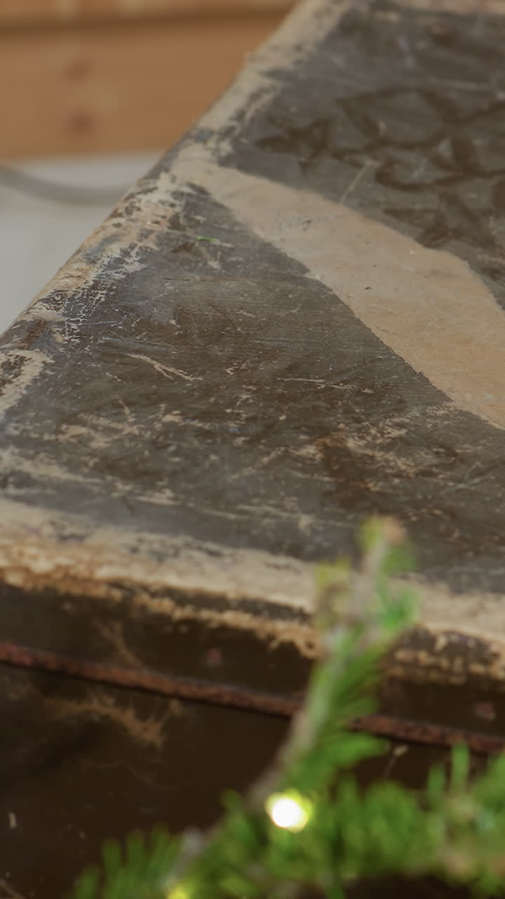 Primer plano de la mano de una mujer caucásica abriendo la tapa de un baúl antiguo; dedos cuidadosos con anillo de boda que revelan pátina y motivos descoloridos, indicios de taller y estudio, ambiente de restauración y conservación, lento