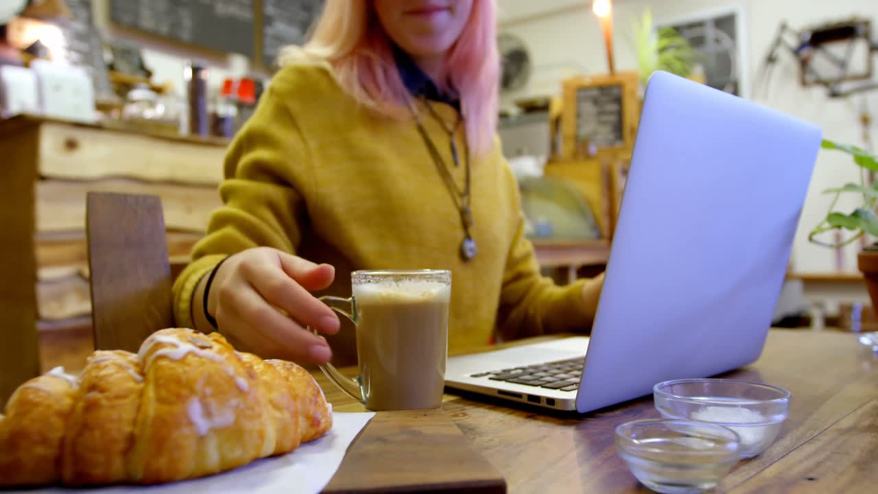 mujer joven hablando por teléfono mientras usa una computadora portátil en un café 4k
