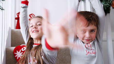 Portrait-Of-Two-Excited-Children-Wearing-Pajamas-Sitting-On-Stairs-Holding-Stockings-On-Christmas-Morning