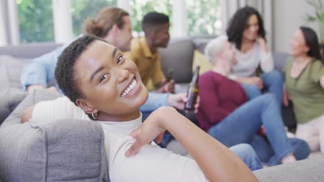Smiling-biracial-woman-sitting-with-diverse-group-of-happy-friends-socialising-in-living-room