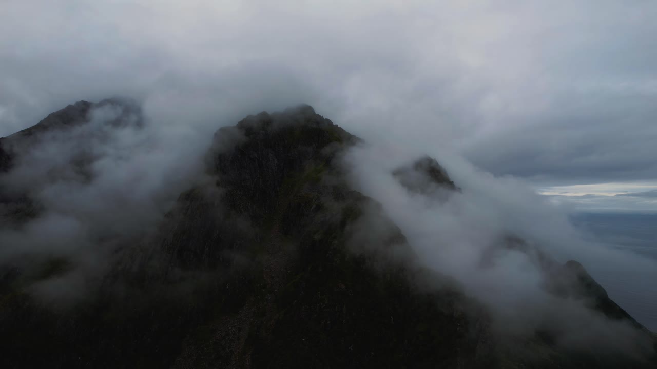 Aerial at cloudy mountain peak. Scenic Lofoten Islands, Norway with deep blue sea and clouds in summer