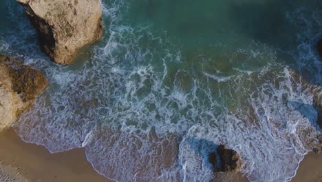 Overhead-aerial-drone-clip-moving-over-a-sandy-beach-and-a-rock-formation-in-Kavala,-Macedonia,-Greece