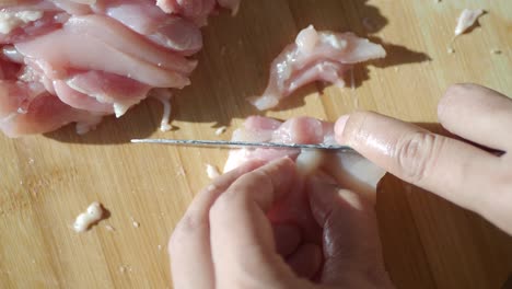 close-up of hands chopping raw chicken breast on a cutting board