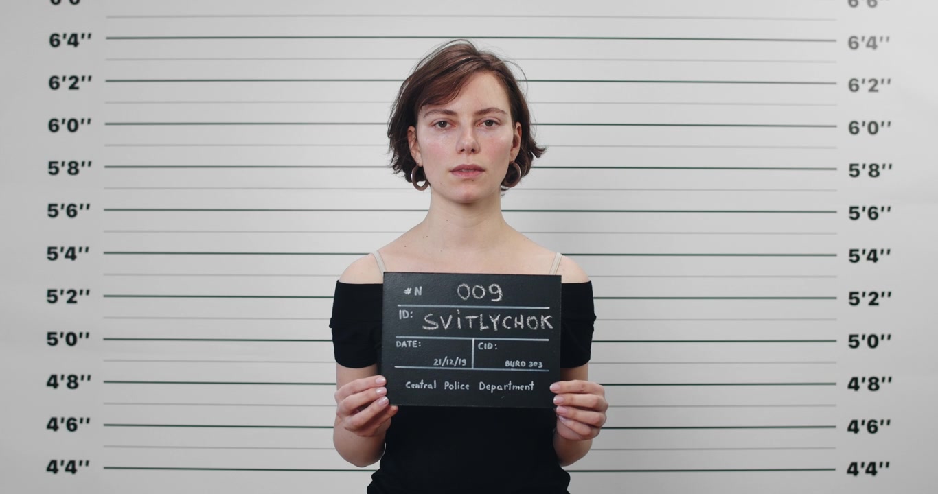 Young Woman Holding Mugshot Board in Police Station