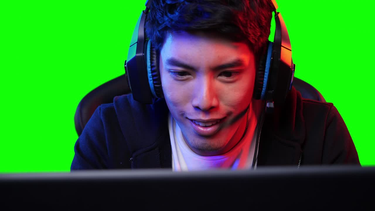 아시안 게이머 남자가 집에서 pc 컴퓨터에서 게임을 하고 화면을 보고 있습니다. 아시안 남자는 마우스와 키보드로 콘솔을 제어합니다. 젊은 남자는 녹색 화면으로 레저 디지털 게임을합니다.