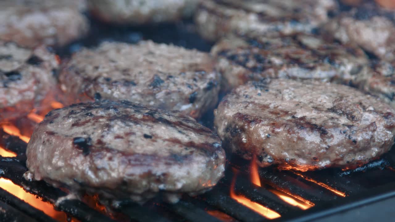 Fiamme che cuociono hamburger di manzo su barbecue rovente