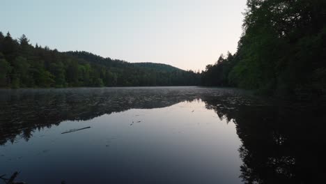 Noch-Klarer-See-Mit-Dem-Himmel-Und-Den-Kiefern,-Die-Sich-Auf-Der-Stillen-Oberfläche-Spiegeln