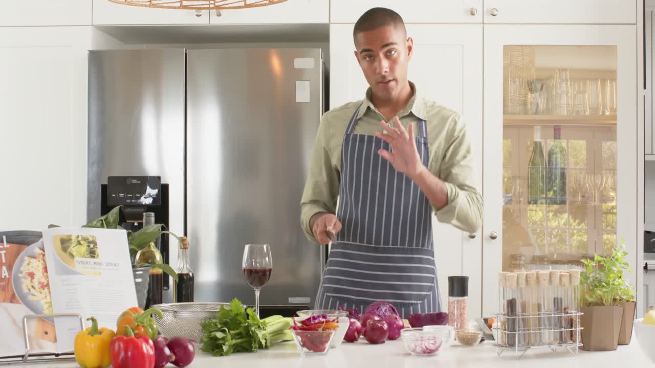 vlogger de cocina masculino biracial en delantal hablando y filmando en la cocina