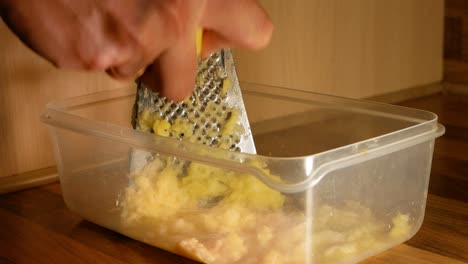 Peeled,-raw-potatoes-being-grated-by-a-married-man-in-homemade-kitche