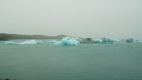 wide pan of blue icebergs floating on lake jokulsarlon on a cloudy day