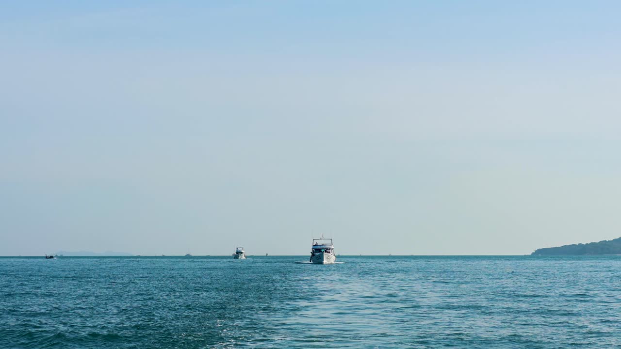 A fishing boat moves steadily across calm waters in Phuket, Thailand, under clear skies with a distant shoreline